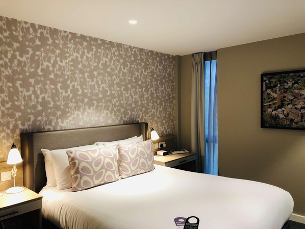 A hotel room with a bed, nightstands, a lamp, a painting, and a view of a cityscape. - Edgbaston Park Hotel & Conference Centre (Birmingham)