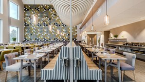 Ein modernes Restaurant mit langen Gemeinschaftstischen, hohen Decken und Wänden mit geometrischen Mustern.