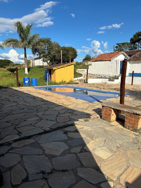 Un patio con piso de piedra, un pequeño edificio amarillo y un edificio blanco con techo rojo.