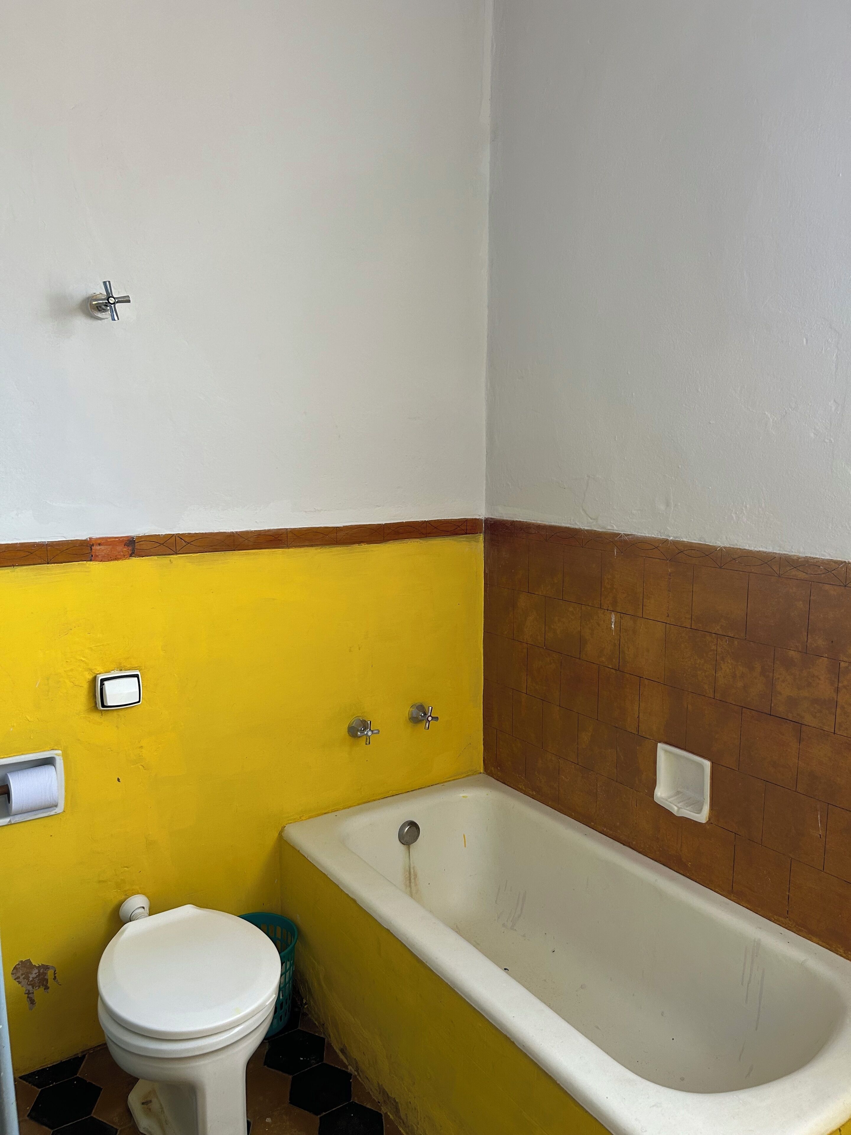 Un baño con una decoración en tonos amarillo y blanco, una bañera blanca, un inodoro blanco y un pequeño cubo de basura.
