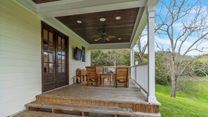 Une véranda en bois avec une table et des chaises, un ventilateur de plafond et une vue sur le paysage environnant.