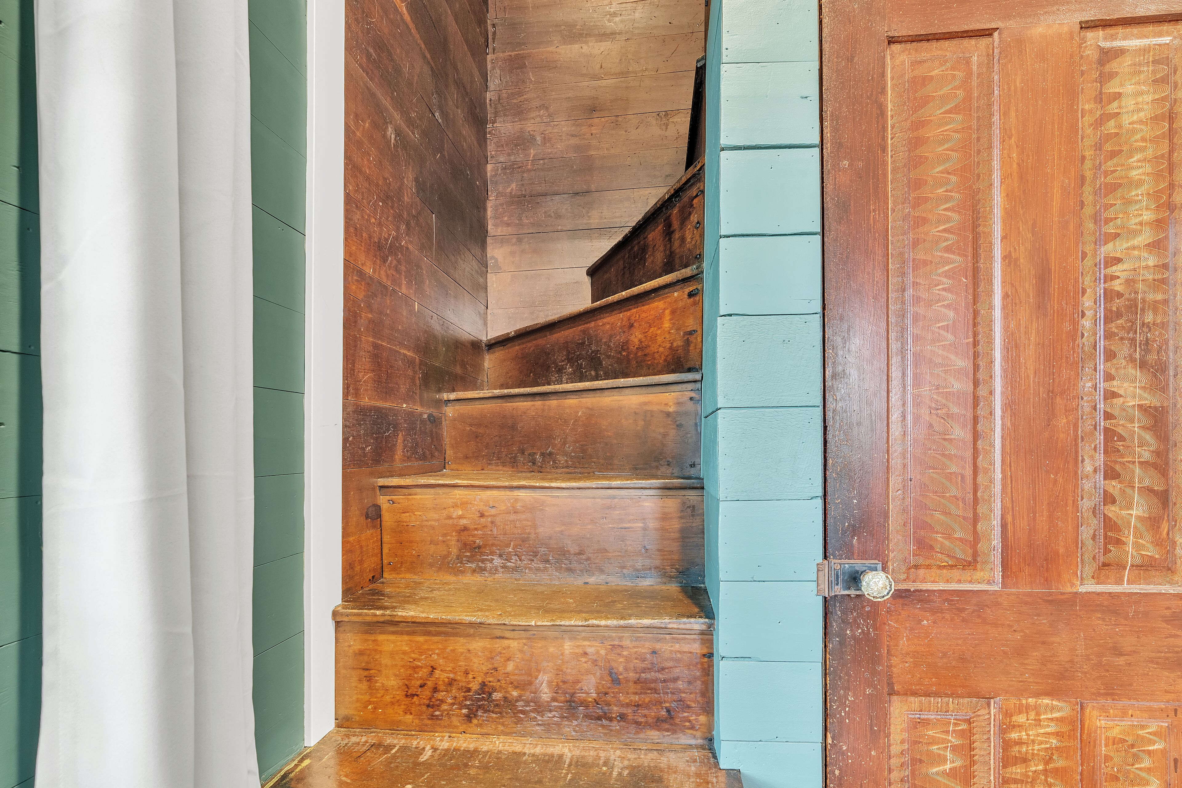 Un escalier en bois avec une rampe et une porte ornée d’un motif décoratif.