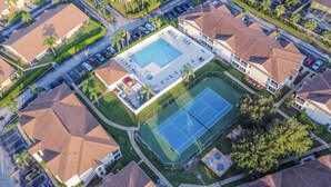 An aerial view of a residential area with a swimming pool, tennis courts, and a parking lot.