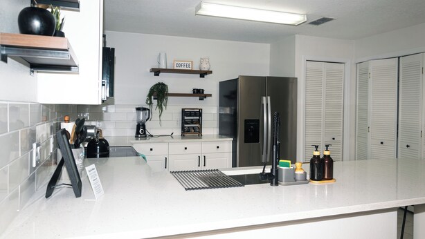 A modern kitchen with white countertops, a stainless steel refrigerator, and a coffee station.