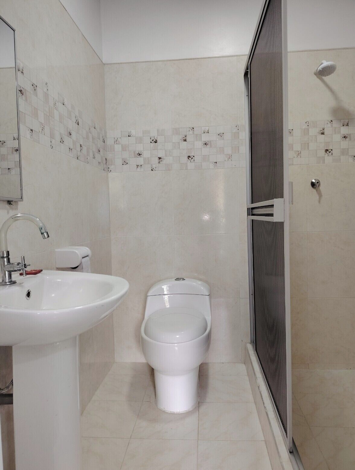 Baño con lavamanos, dos inodoros y zona de ducha.