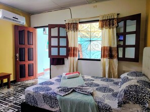 A room with a bed, a wooden door, an air conditioning unit, and a window with decorative curtains. - Hotel Alto Amazonas  (Leticia)