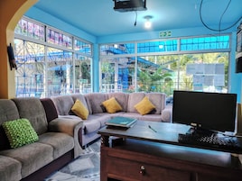 Una habitación con sofá, escritorio con computadora y ventanas amplias con barrotes de metal.
