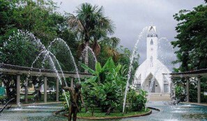 A church with a white facade and a bell tower, surrounded by a fountain and lush greenery. - Hotel Alto Amazonas  (Leticia)