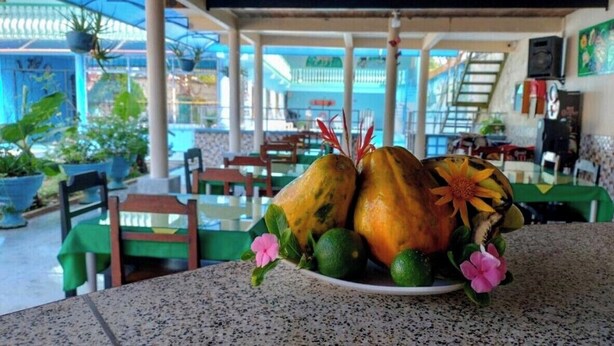 A dining area with a table set for two, featuring a plate with a fruit arrangement and a flower. - Hotel Alto Amazonas  (Leticia)
