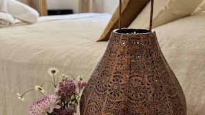A bedroom with a bed, a small table with a decorative lamp and a vase of flowers, and a window with a view of trees. - Agroturismo Sa Marina Ibiza (Santa Eulalia del Rio)