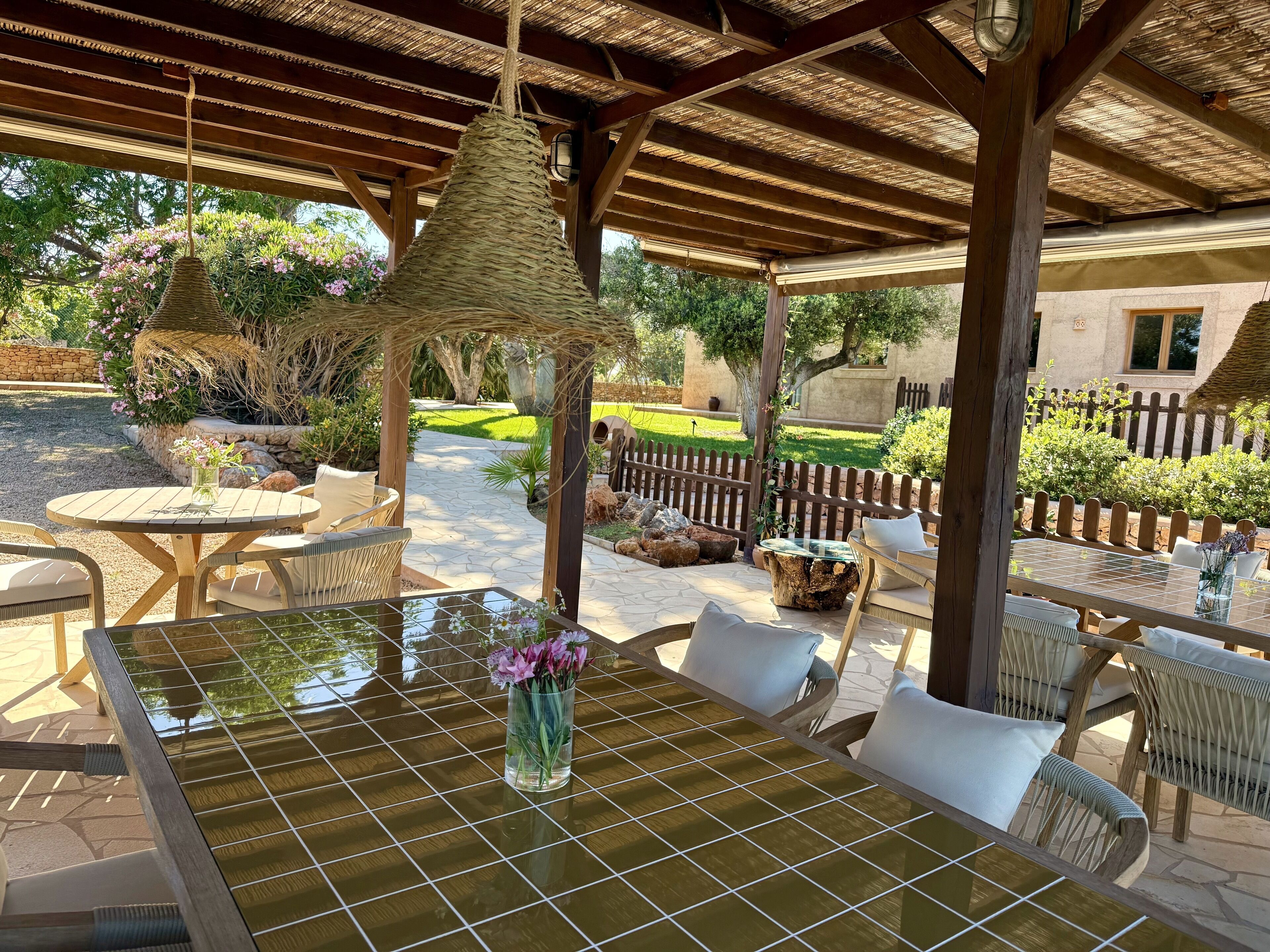 An outdoor patio with a glass-top table, wicker chairs, and a hanging light fixture.