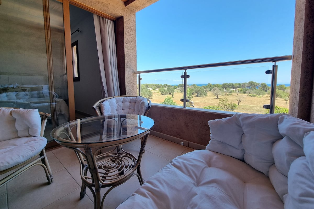 Un balcon doté d’une table en verre et de chaises en osier, offrant une vue sur un paysage magnifique.