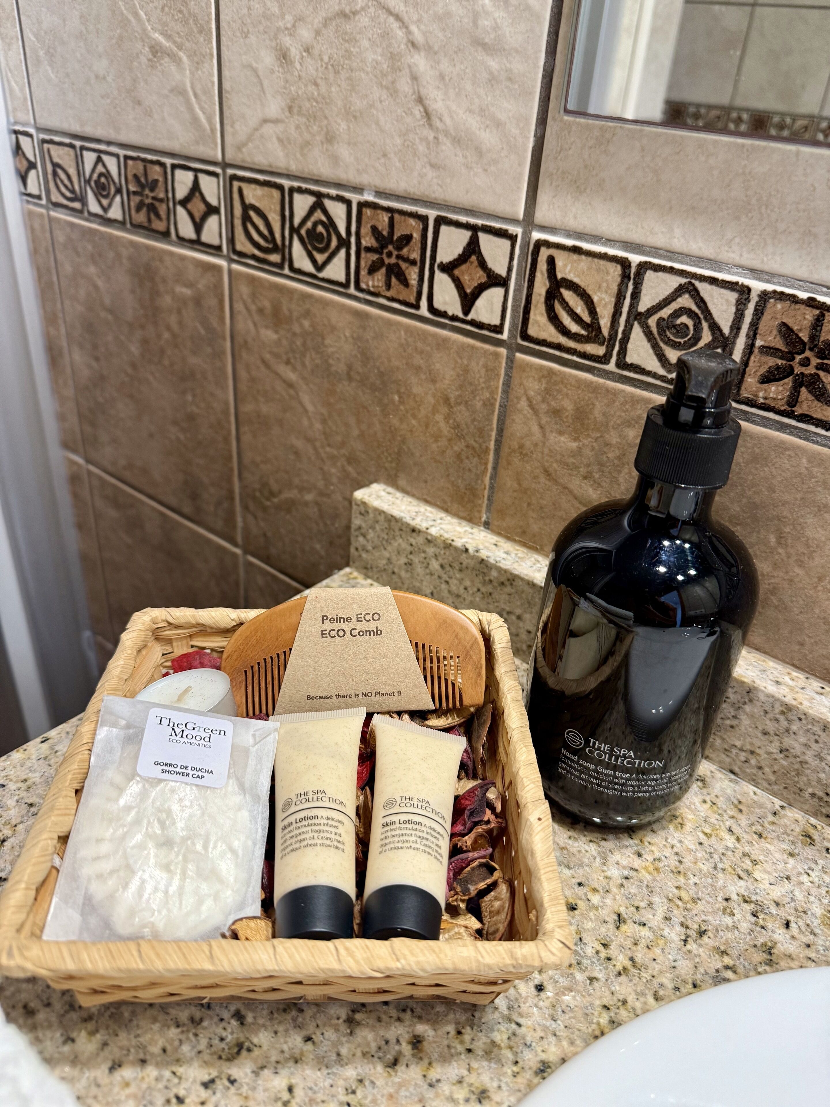Une salle de bain avec un mur recouvert de carreaux, un panier en bois contenant des articles de toilette et un flacon de savon pour les mains.