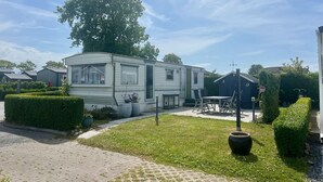 A mobile home with a paved driveway, a small patio area, and a well-maintained lawn. - ZP 360 - Camping de Zandput (Vrouwenpolder)