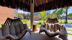 Un espace extérieur aménagé, abrité et doté de chaises confortables et d’une table en bois, offrant une vue sur une piscine et un espace verdoyant.