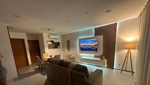 Un salon moderne doté d’un grand téléviseur à écran plat, d’un canapé, d’un coin repas et d’un lampadaire.