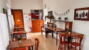 A dining area with wooden tables and chairs, a ceiling fan, and a kitchen in the background. - Hotel Veleiro (São Sebastião)