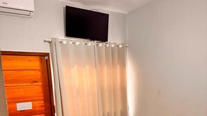 A small, clean room with a wooden door, a bed with a white bedspread, a small bedside table, and a ceiling fan. - Hotel Veleiro (São Sebastião)