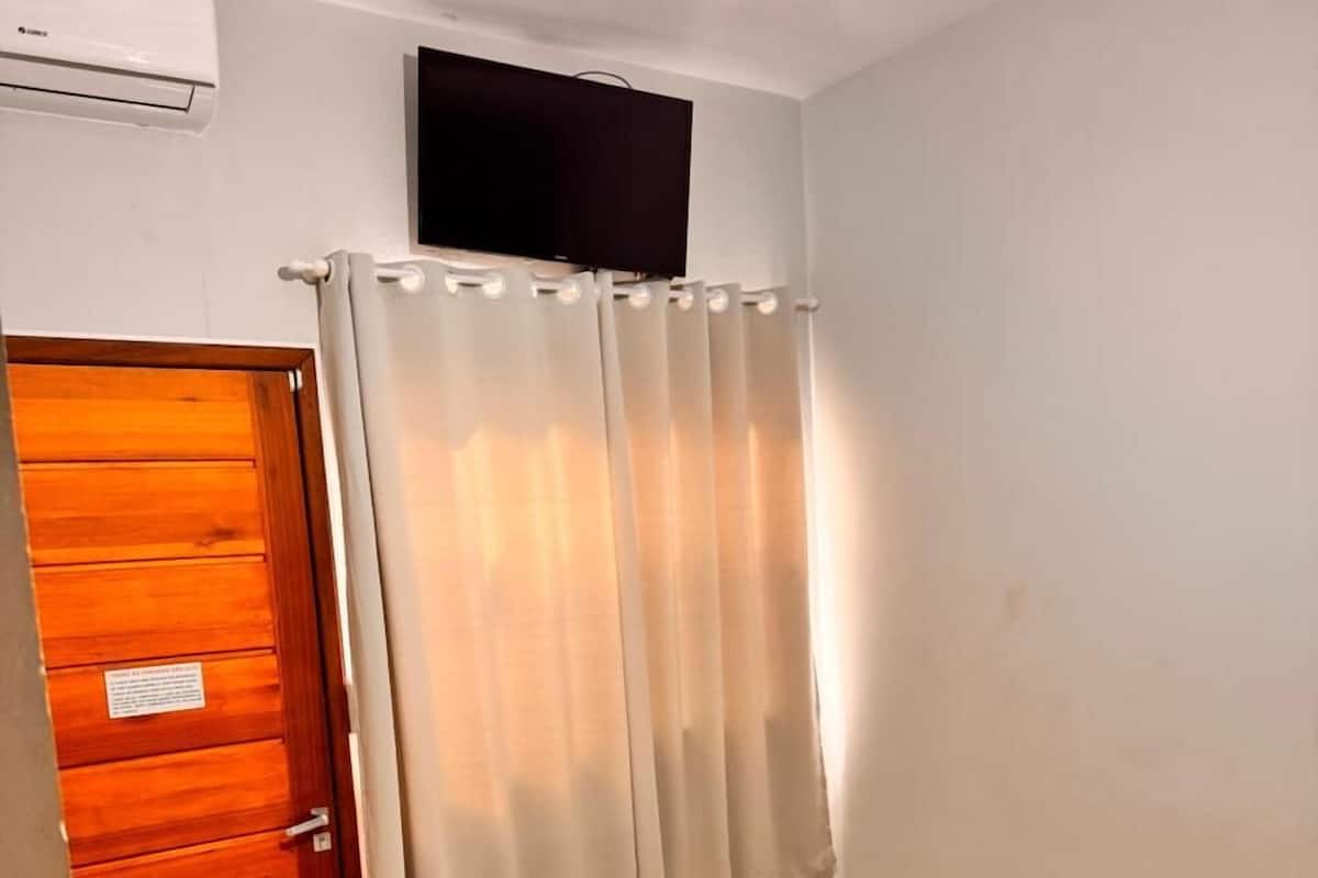 A small, clean room with a wooden door, a bed with a white bedspread, a small bedside table, and a ceiling fan.