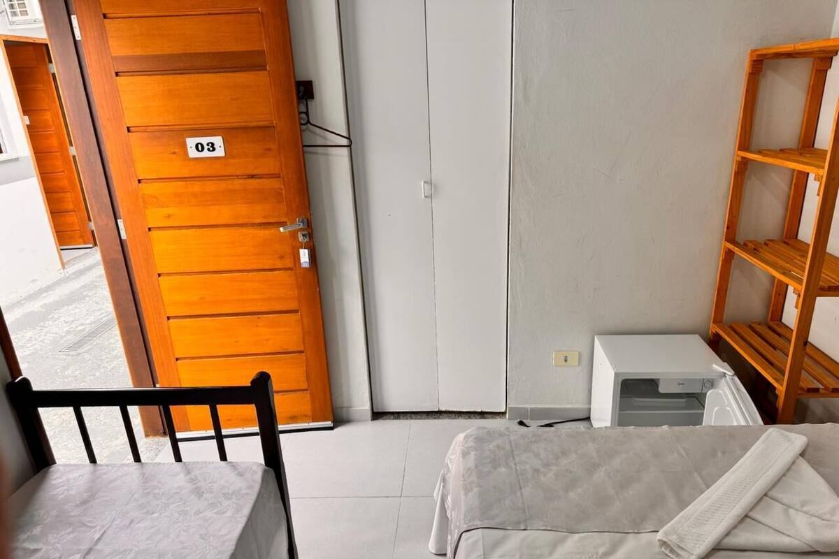 A room with a bed, a wooden chair, a wardrobe, and a small white appliance, likely a heater or air conditioner.