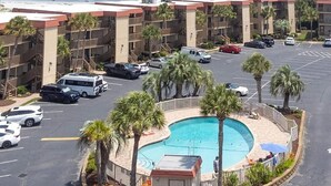 Ein Hotel mit Pool, umgeben von Palmen, einem Parkplatz mit mehreren Autos und Blick auf den Ozean.