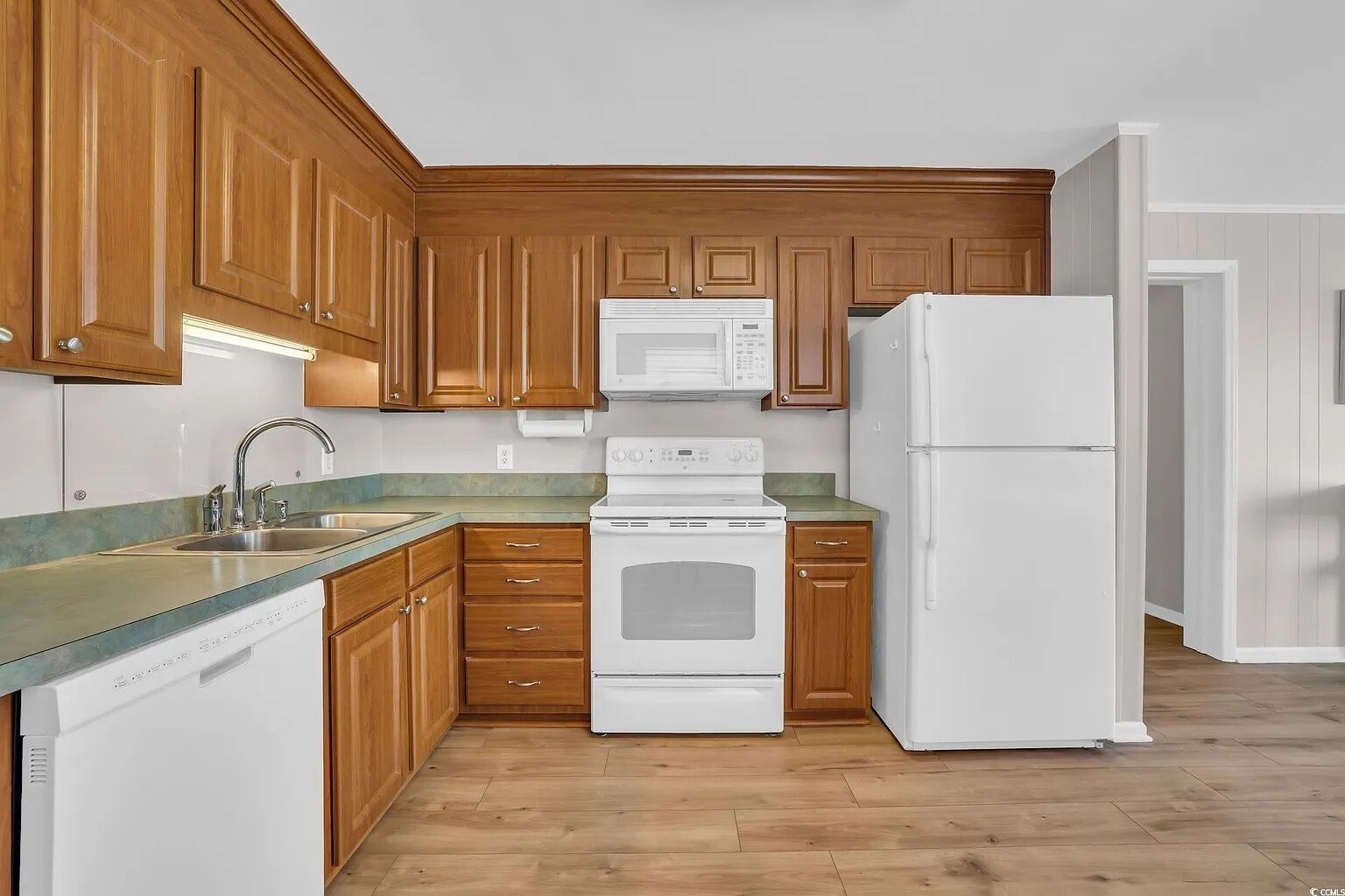 A kitchen with wooden cabinets, a white stove, a microwave, a sink, and a refrigerator.