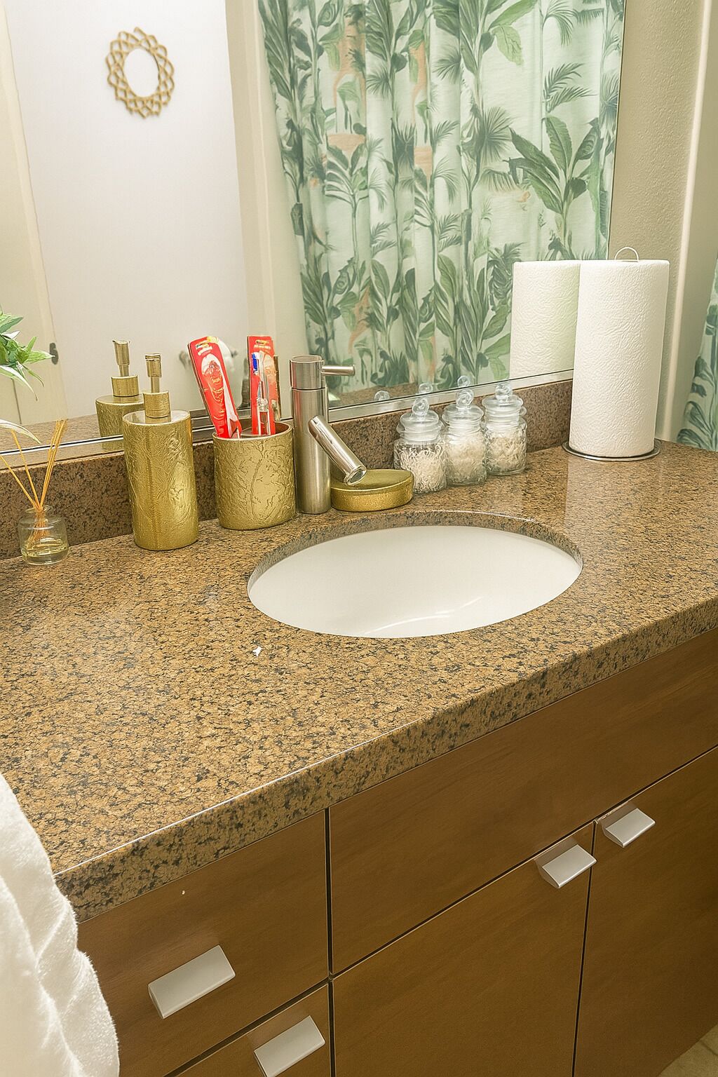A bathroom with a granite countertop, a white sink, and gold-colored toiletries.