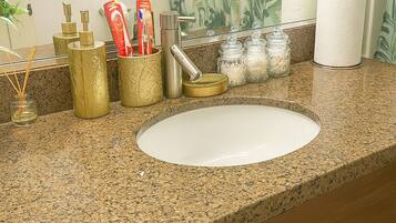 A bathroom with a granite countertop, a white sink, and gold-colored toiletries.