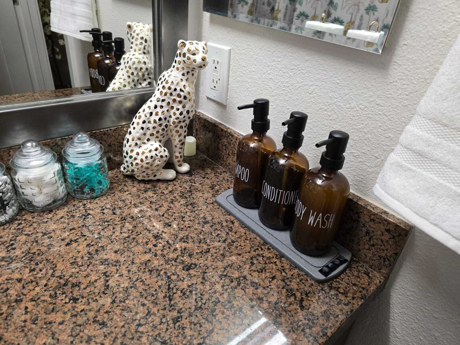 A bathroom counter with a leopard figurine, three bottles of shampoo and conditioner, and two glass jars with white and blue contents.