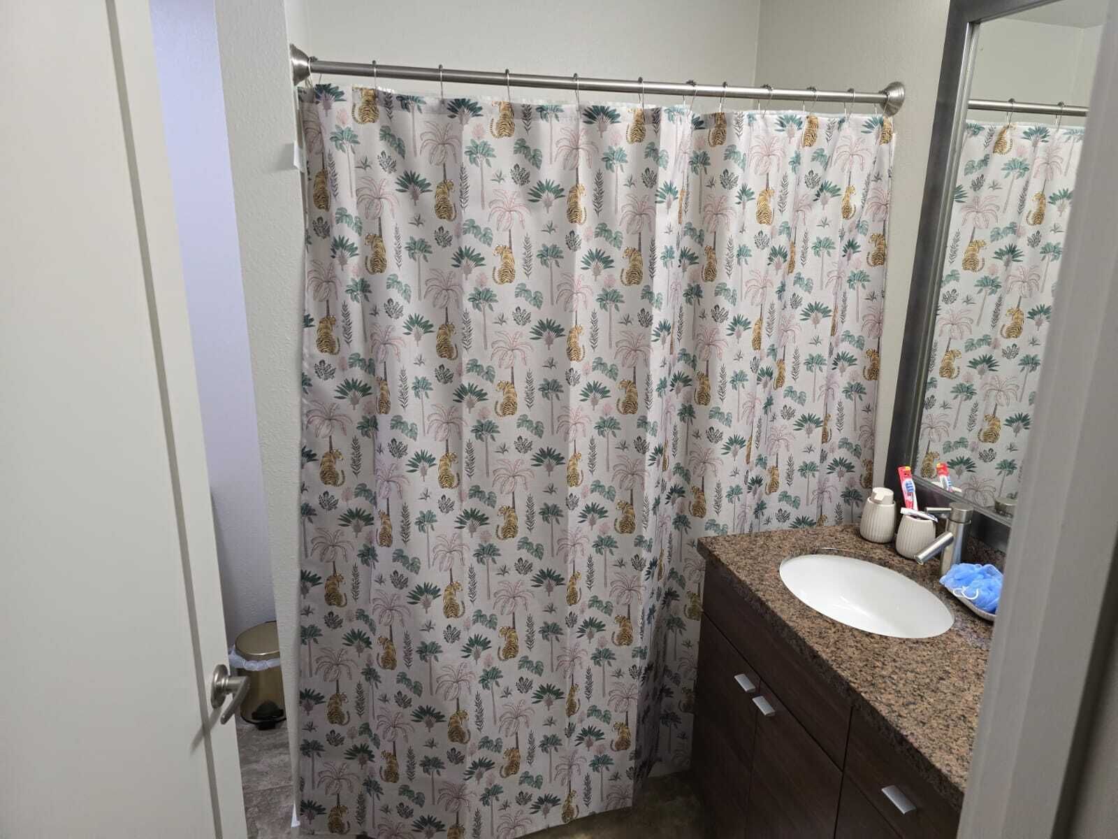 A bathroom with a shower curtain featuring a tropical pattern, a white sink, and a mirror.