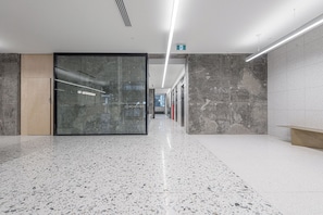Um corredor moderno com piso de terrazzo, uma porta de vidro com a inscrição "DORCHESTER" e um banco à direita.