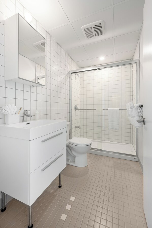 A modern bathroom with a white vanity, a toilet, and a glass-enclosed shower.