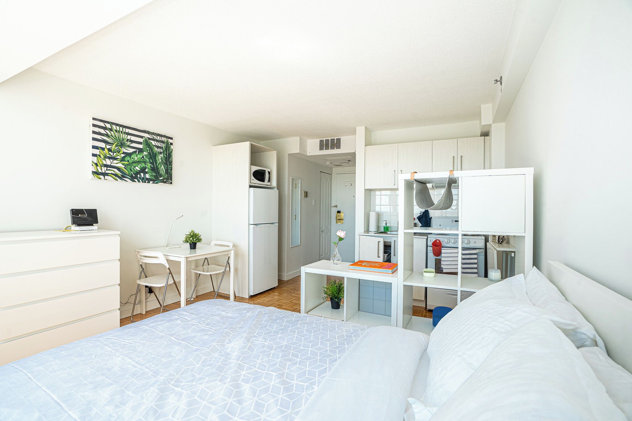 A modern, compact bedroom with a bed, desk, and kitchenette.