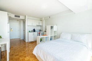 Quarto com cama, escrivaninha e cozinha compacta.