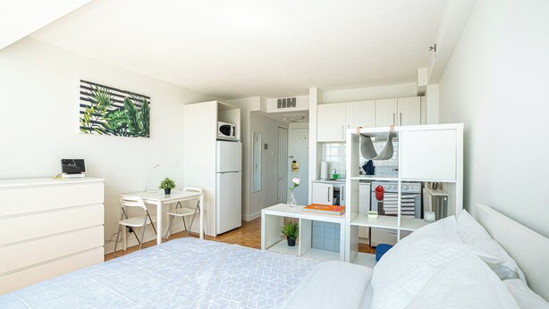 Een moderne, compacte slaapkamer met een bed, bureau en kitchenette.