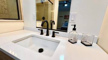 Een moderne badkamer met een witte wastafel, zwarte kraanwerk en een glazen zeepdispenser.