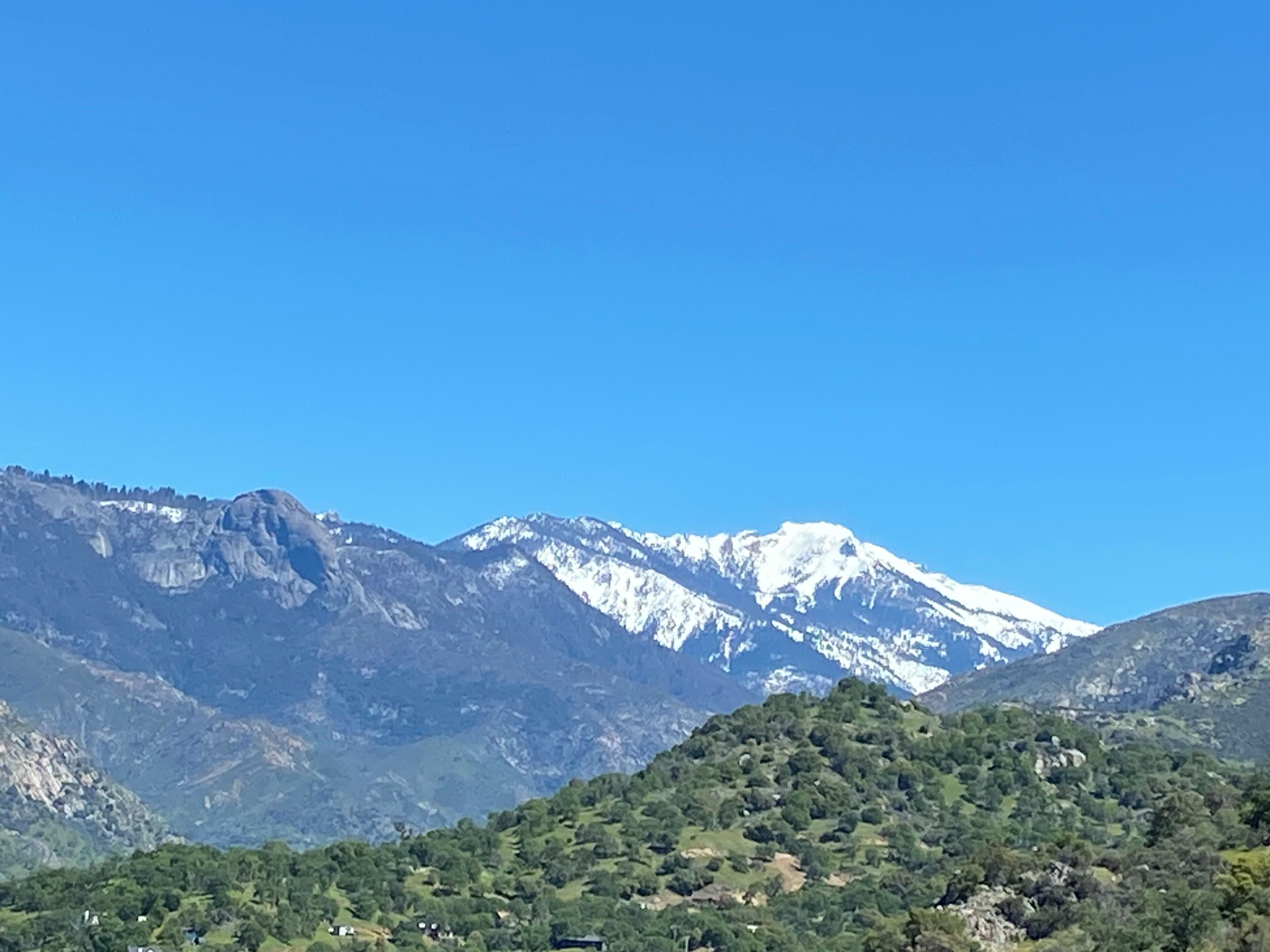 A mountainous landscape with snow-capped peaks and a forested hill in the foreground.