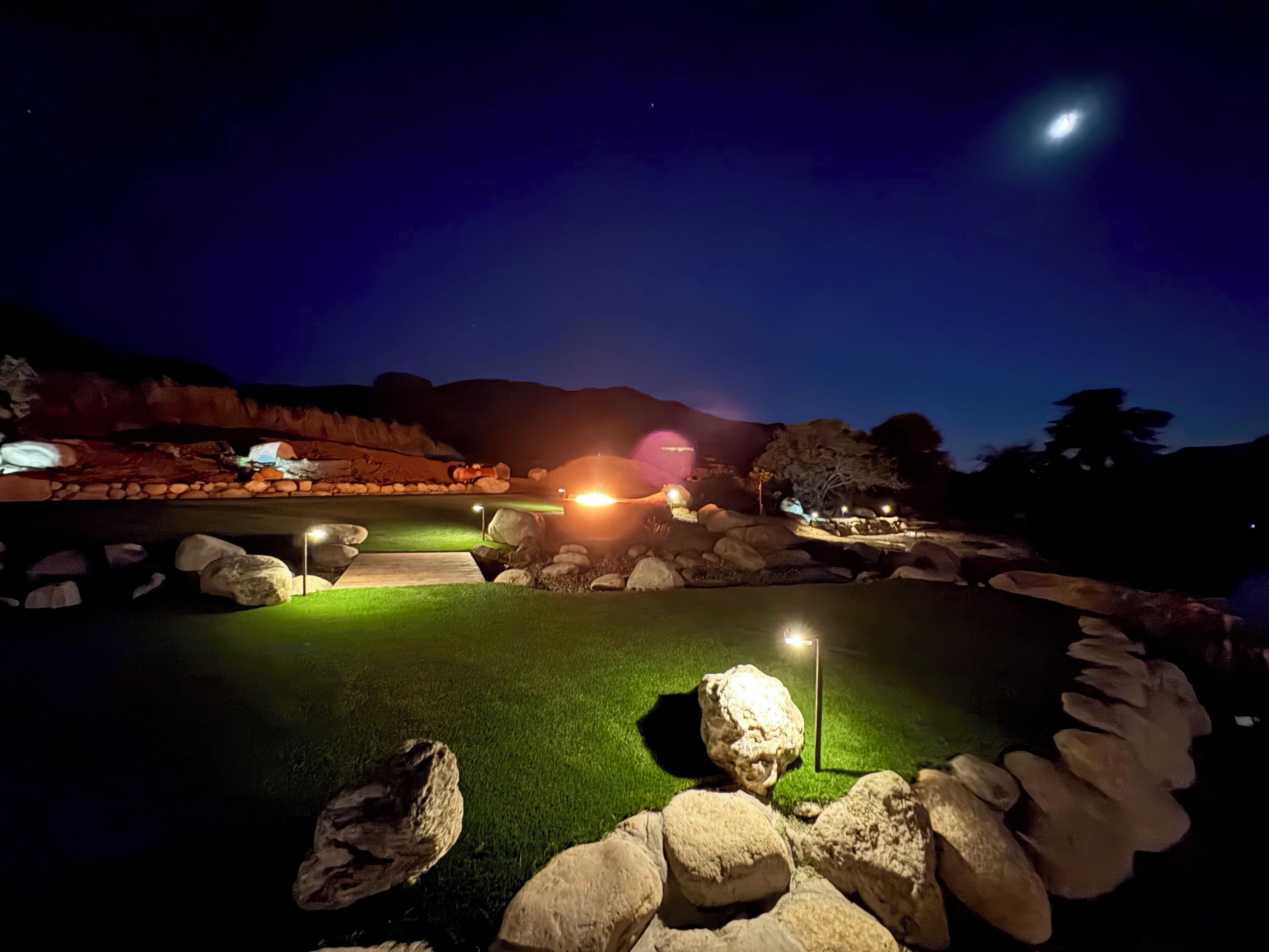 Un parcours de golf nocturne, illuminé par des projecteurs, doté d’un gazon bien entretenu et bordé de rochers.