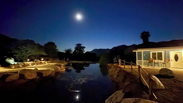 A nighttime view of a lakeside area with a building featuring a covered deck and seating area.