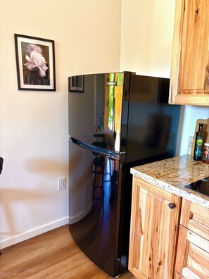 A kitchen with a stainless steel refrigerator, wooden cabinets, a marble countertop, and a framed picture on the wall.