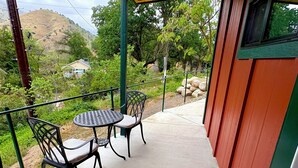 A covered patio with a table and chairs, overlooking a hillside with greenery and a house in the background. - Spacious and unique Studio suite in  enchanting Three Rivers with WiFi, AC (Three Rivers)