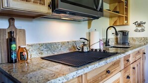A kitchen with wooden cabinets, a granite countertop, a kettle, a coffee maker, and a cutting board with a bottle of honey and a jar of honey. - Spacious and unique Studio suite in  enchanting Three Rivers with WiFi, AC (Three Rivers)