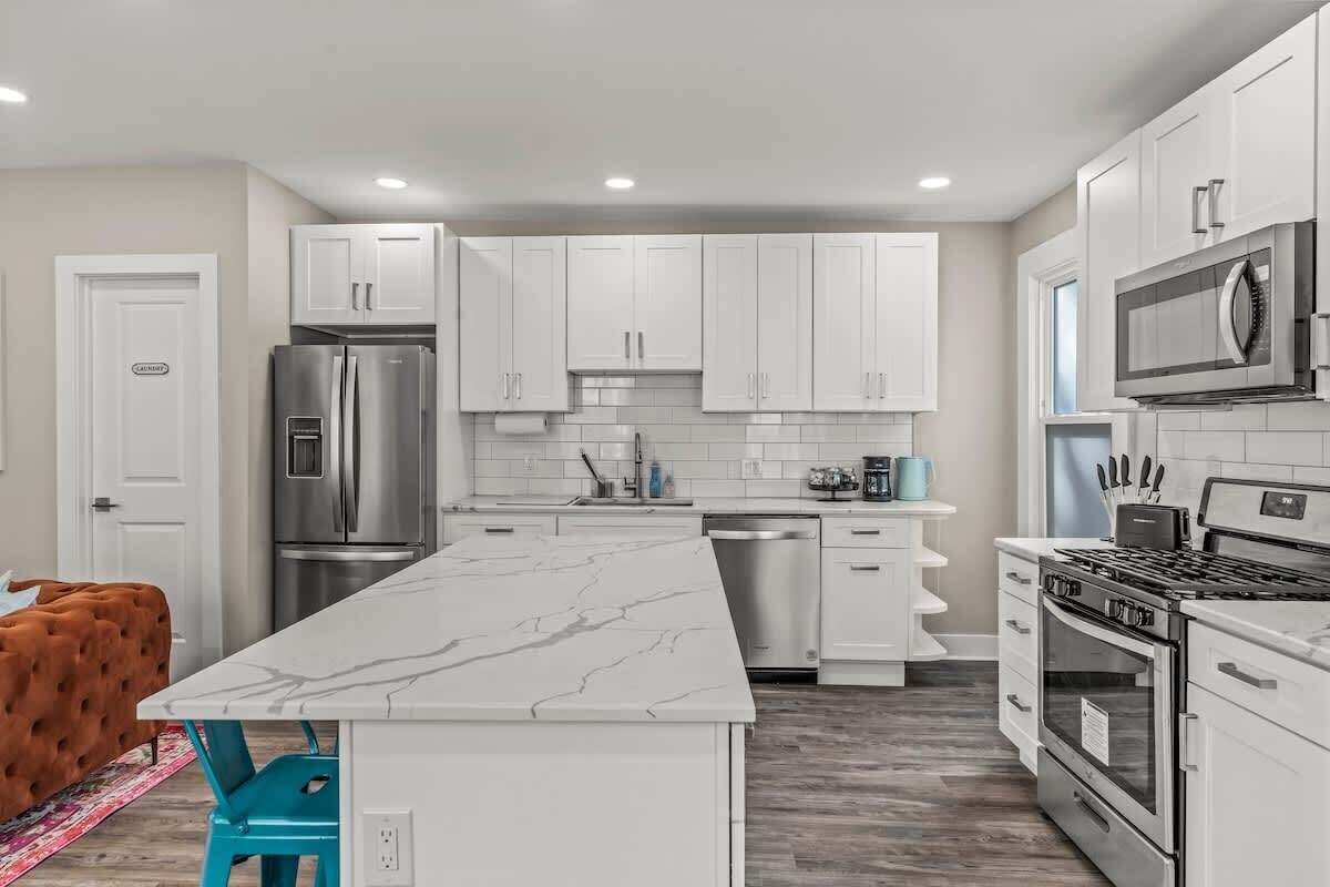 A modern kitchen with white cabinets, stainless steel appliances, and a marble countertop.