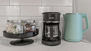 A kitchen with a coffee maker, a teal mug, and a tray with jars.