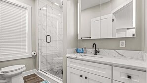 A bathroom with a toilet, shower, and vanity with drawers.