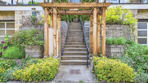 Una pérgola de madera con una escalera que conduce a un edificio de piedra.