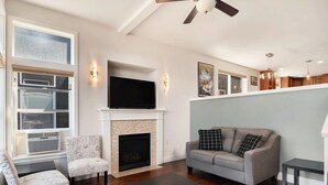 Una sala de estar moderna con chimenea, televisor de pantalla plana, ventilador de techo y sofá con cojines estampados.