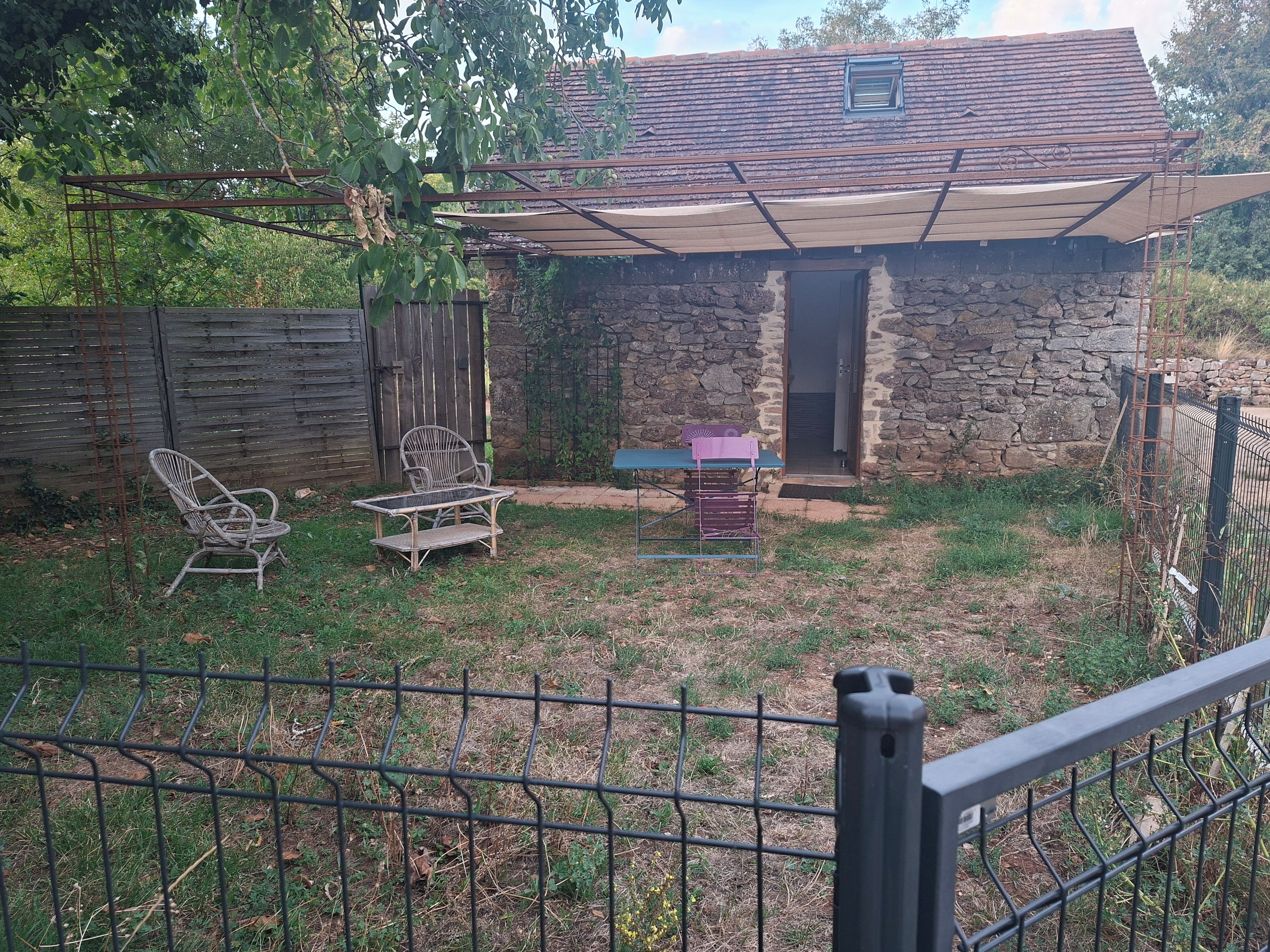 Une maison en pierre avec un patio couvert, une clôture en bois et du mobilier d’extérieur.