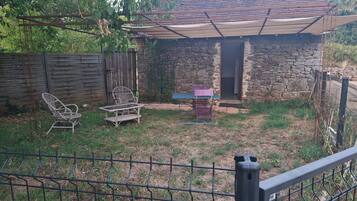 Une maison en pierre avec un patio couvert, une clôture en bois et du mobilier d’extérieur.