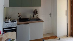 A compact kitchen with wooden beams, a stove, a sink, and green cabinets. - Gîte/Studio sleeps 2 with enclosed garden (pets welcome) and large shower. (Loubressac)